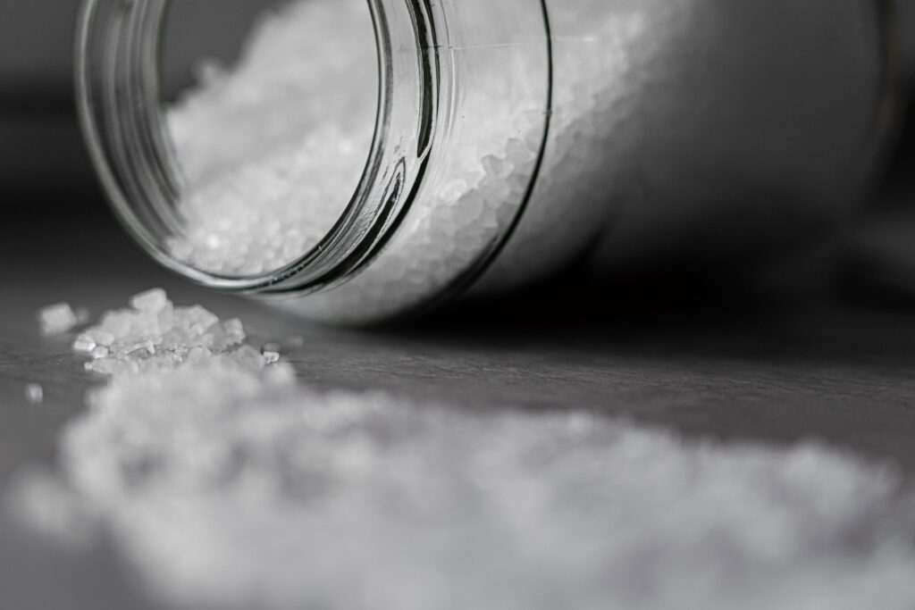 Coarse rock salt spilling from a glass jar, used for cleaning glass pieces